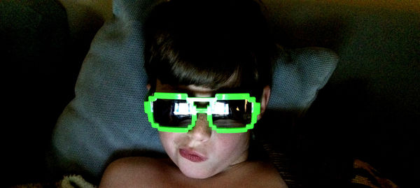 Portrait of cute boy with green sunglasses lying on bed