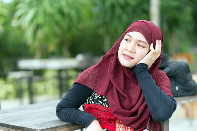 Woman looking away while sitting at table against trees
