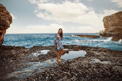 Rear view of woman standing at beach against sky