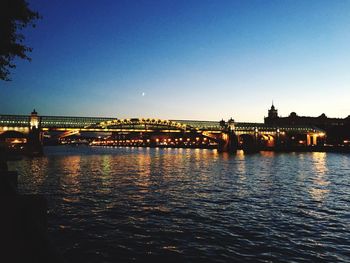 Illuminated bridge over river against clear blue sky