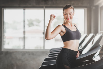 Portrait of smiling young woman standing on treadmill at gym