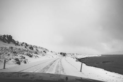 Snow covered road seen through car windshield against cloudy sky