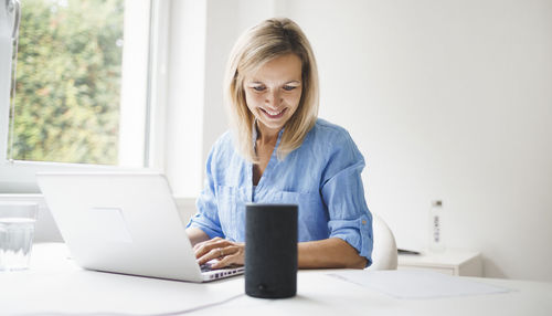 Smiling woman using laptop while sitting by table at office