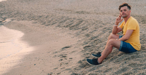 Full length of young woman sitting on sand at beach