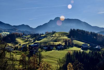 Scenic view of fields with farm houses and trees against mountains and sky