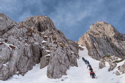 Low angle view of people climbing snow covered mountain