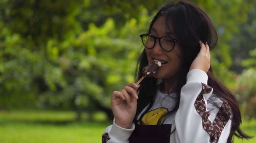 Smiling young woman eating ice cream while standing outdoors