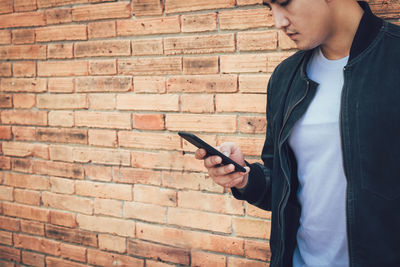 Man using mobile phone against brick wall