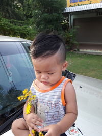 Cute baby boy holding flower while sitting on car bonnet