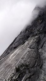 Low angle view of rocky wall against clouds