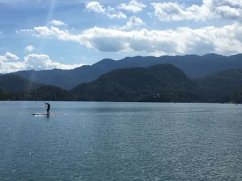 Scenic view of person paddle boarding on lake and mountains against sky