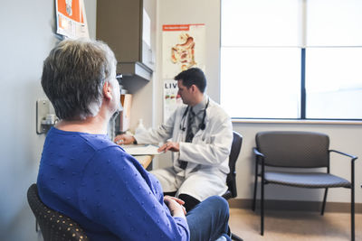 Doctor taking patient history from older woman at a desk in a clinic.