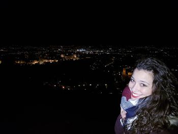 Portrait of smiling woman against illuminated cityscape against sky at night