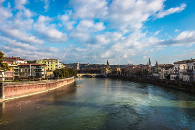 Arch bridge over river amidst buildings in city against sky