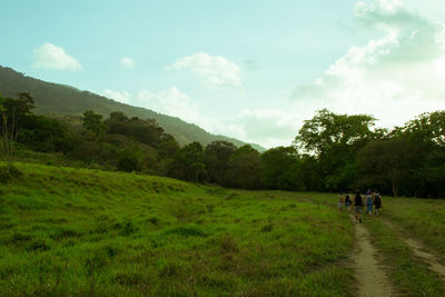 People walking on pathway at grassy field against sky