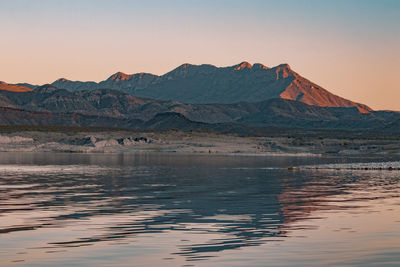 Scenic view of lake by mountains against sky during sunset