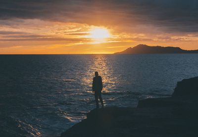 Man standing at beach against sky during sunset