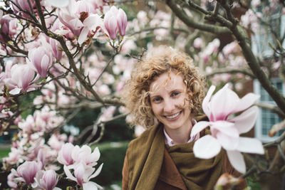 Portrait of smiling woman with curly hair amidst cherry blossom