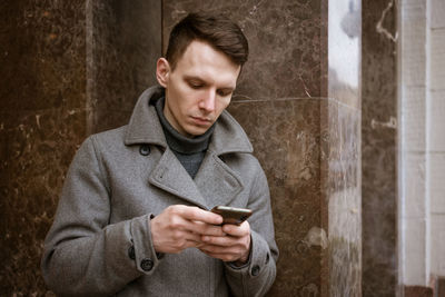 Close-up shot fashionable young man using his mobile phone, wearing man's coat