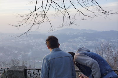 Rear view of two men looking down while standing by railing against sky