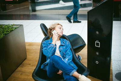 Young woman sitting on chair while talking on mobile phone