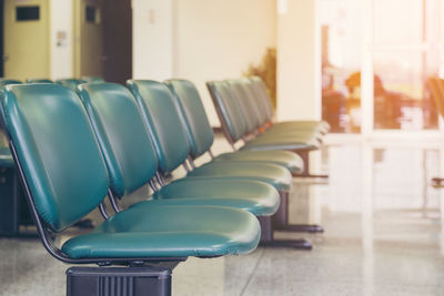 Empty seats at a business or the chairs are green leather with metal legs and no armrests waiting