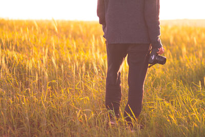 Rear view of man holding camera and standing on grassy field
