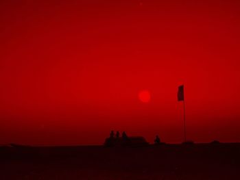 Silhouette people on field against orange sky