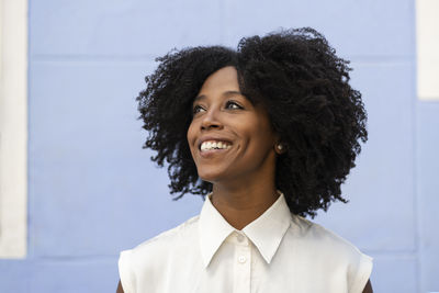 Thoughtful smiling woman with afro hairstyle in front of wall