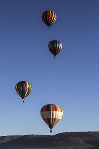 Colorful hot air balloons flying over mountain against clear blue sky