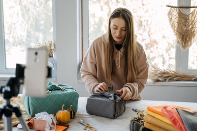 Smiling woman holding gift box blogging at home