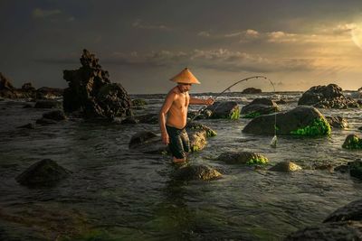 Man standing on rock by sea against sky