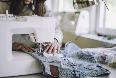 Midsection of female design professional stitching fabric through sewing machine at workshop