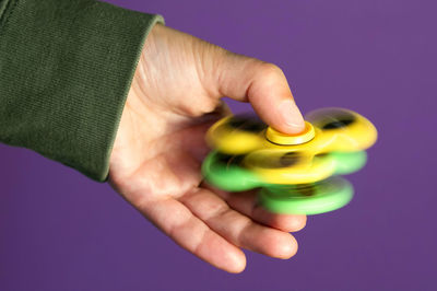 Close-up of cropped hand spinning fidget against purple background