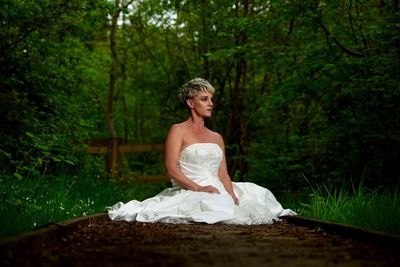 Bride sitting on dirt road while looking away in forest