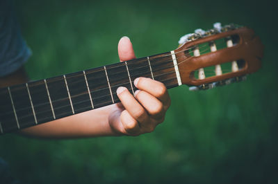 Cropped hand of person playing guitar over field