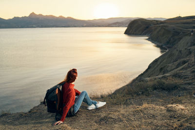 Man sitting on rock by mountain against sky