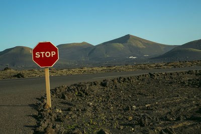 Stop sign by road against clear blue sky