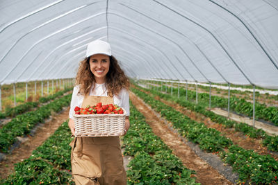 Portrait of smiling young woman holding basket in greenhouse