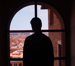 Rear view of silhouette man looking through window