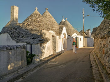 Rear view of woman walking by building against sky, in alberobello, apulia, italy 