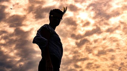 Low angle view of man against cloudy sky during sunset