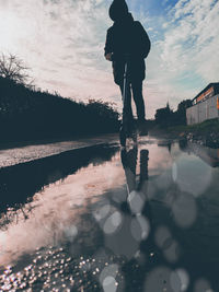 Rear view of silhouette man standing by lake against sky during sunset