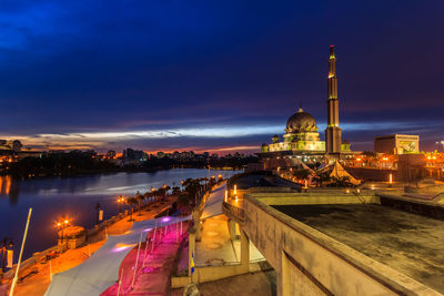 Illuminated city by river against sky at night