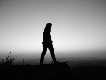 Silhouette man standing on rock against clear sky