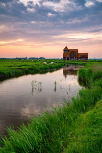 Scenic view of lake by building against sky during sunset