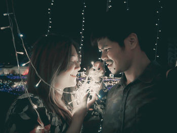 Couple standing by illuminated string lights at night