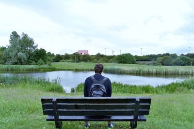 Rear view of man sitting on lake against sky