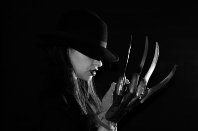 Portrait of young woman holding hat against black background