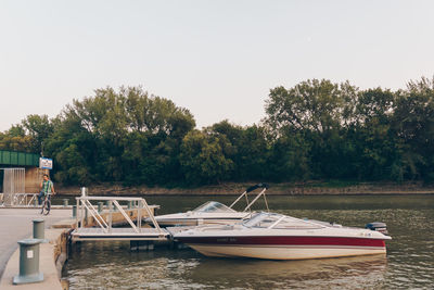 Boats moored on river by trees against clear sky